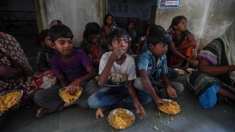 Un grupo de niños de uno de los refugios habilitados se disponen a comer los alimentos distribuidos por una ONG tras el paso del 'ciclón Vayu' este jueves en Veraval (India). | EFE