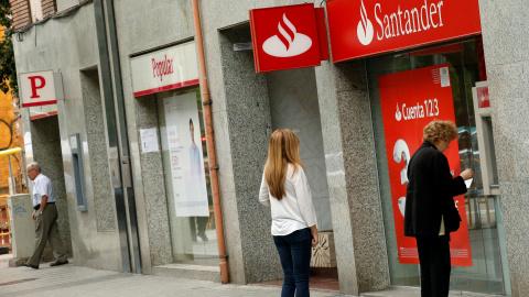 Un par de personas utilizan un cajero automático de una oficina del Banco Santander, en Barcelona, situada junto a una sucursal del Popular. REUTERS/Albert Gea