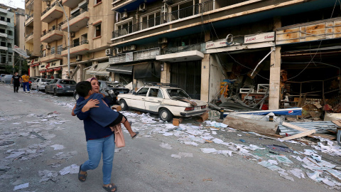 Una mujer lleva a un niño mientras pasa por las tiendas dañadas tras la explosión del martes en Beirut, Líbano