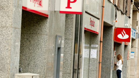 Una mujer usa un cajero automático en una oficina del Banco Santander junto a una sucursal del Banco Popular. REUTERS/Albert Gea