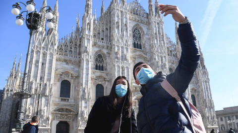 Dos turistas con mascarilla se hacen una fotografía junto a la catedral de Milán. - EFE