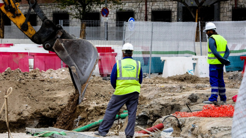 Dos trabajadores a pie de calle y otro en el tractor, en una obra en Madrid. E.P./Jesús Hellín