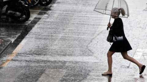 Una mujer cruza un paso de cebra bajo la lluvia. EFE/Archivo.