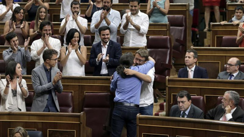 El líder de Podemos, Pablo Iglesias (de espaldas), abraza al portavoz de En Comú Podem, Xavier Domènech, tras su intervención en la segunda sesión del debate de investidura del líder del PP, Mariano Rajoy, esta mañana en el Congreso de los Diputado