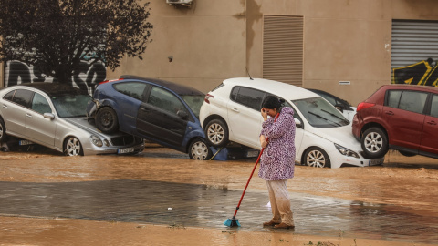  Una mujer realiza labores de limpieza junto a vehículos destrozados tras el paso de la DANA por el barrio de La Torre de València - EP