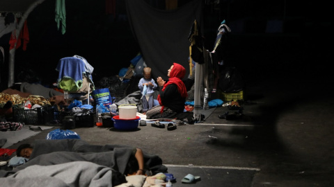 Una mujer reza mientras refugiados y migrantes del destruido campamento de Moria encuentran refugio en el estacionamiento de un supermercado. REUTERS / Elias Marcou