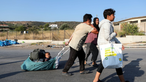 Un hombre tira de un bebé mientras los refugiados y migrantes de la destruida Moria se dirigen hacia un nuevo campamento temporal durante una operación policial, en la isla de Lesbos. REUTERS / Elias Marcou