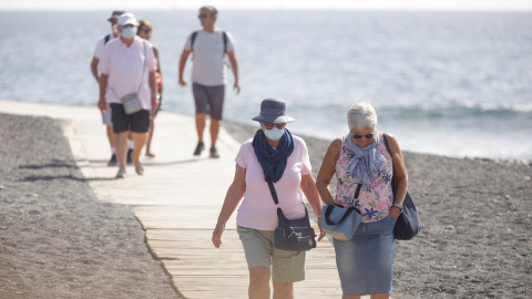 Varios turistas pasean este viernes por las inmediaciones del hotel en el que desde el pasado lunes permanecen incomunicados sus huéspedes y trabajadores al dar positivo en coronavirus cuatro de los que se alojaban en el centro turístico de Adeje, en el