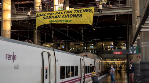 Activistas de Greenpeace han desplegado esta mañana una pancarta sobre las vías de Atocha para denunciar la falta de trenes en un verano marcado por la crisis de la covid-19. Bajo el texto "Ábalos: faltan trenes, sobran aviones". EFE/Pablo Blázquez