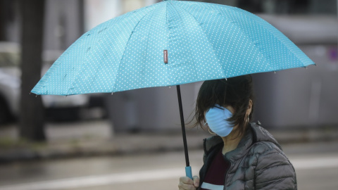 Una mujer protegida con mascarilla y guantes se resguarda de la lluvia bajo su paraguas. María José López / Europa Press / Archivo