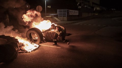 Un trabajador de Alcoa alimenta el fuego de la barricada con un neumático a la entrada de la factoría en San Cibrao. MANU BRABO