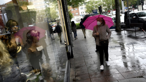 Una mujer pasa frente a una tienda con un paraguas un día de lluvia y bajada de temperaturas en toda España. Óscar Cañas / Europa Press / Archivo