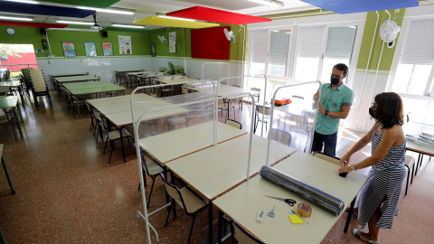 Xavi Leal y Carolina Ramos, director y jefa de estudios, respectivamente, del CEIP Jaume I de Catarroja, colocan los parabanes, realizados con unos percheros y una lámina de plástico transparente, para prepararse para la vuelta a las aulas en la Comunit