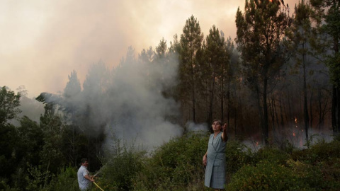 Dos habitantes de Louriceira intentan apagar un foco cerca de su pueblo. | MIGUEL VIDAL (EFE)