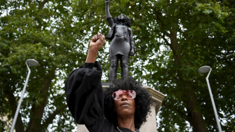 La manifestante Jen Reid con el puño en alto posa frente a una representación de sí misma, la estatua 'A Surge of Power (Jen Reid)' del artista británico Marc Quinn. EFE / EPA / NEIL HALL