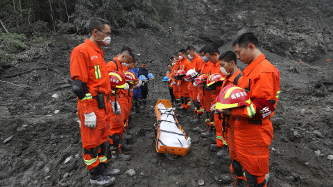 Trabajadores de rescate chinos rinden un minuto de silencio ante el cuerpo de una de las victimas del alud que sepultó una aldea del Tibet./REUTERS