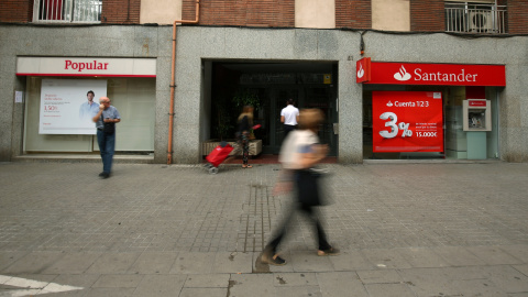 Varios personas pasan junto a sendas oficinas de Banco Popular y Banco Santander, en Barcelona. REUTERS/Albert Gea