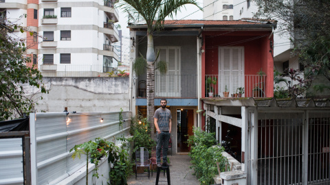 Gustavo posando en frente de la casa que empezó a rentar en el verano de 2015 en Vila Madalena. Las casas cercanas fueron demolidas hace 1 mes y las torres serán construidas en 6 meses. Convenció al propietario de alquilarle la casa en lugar de venderl