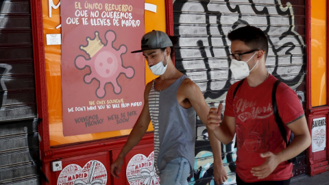 MADRID, 04/08/2020.- Dos jóvenes pasan ante un cartel alusivo al coronavirus en el centro de Madrid, este martes 4 de agosto, EFE/Mariscal