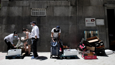 Dos personas recogen alimentos que les dan dos voluntarios a las puertas de la Parroquia Santa María Micaela donde han acudido para recibir una ayuda alimentaria. Eduardo Parra / Europa Press / Archivo