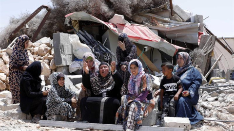 17/06/2019.- Una familia palestina permanece sentada cerca de los escombros de su casa tras ser demolida por las fuerzas israelíes, este lunes, en Yatta, al sur de Hebrón. El ejército israelí destruye las casas de aquellos palestinos que no tienen los