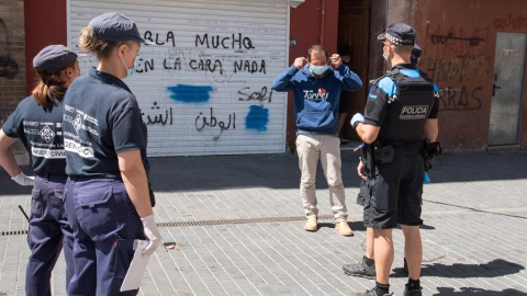 Agentes cívicos (i) y de la Guardia Urbana (d) entregan una mascarilla a un hombre que no llevaba, este jueves, cuando se han puesto en marcha las medidas especiales de restricción de movimientos. /EFE