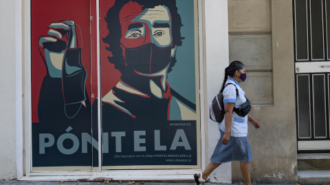 Una mujer pasa junto a una pancarta en la que se ve a Fernando Simón fomentando el uso de la mascarilla.- AFP