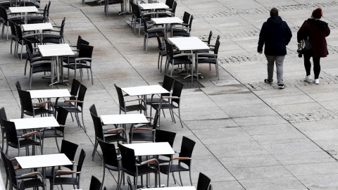 22/10/2020.- Dos personas caminan por la Plaza del Castillo de Pamplona que hoy jueves presenta un inusual aspecto con las terrazas de los bares vacías en una jornada en la que cientos de pamploneses salen este día "Juevintxo", para compartir en la call