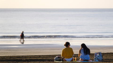 Dos jóvenes charlan en la playa de Maspalomas, en el sur de Gran Canaria, este martes a primera hora de la mañana, en un día con el cielo totalmente despejado.