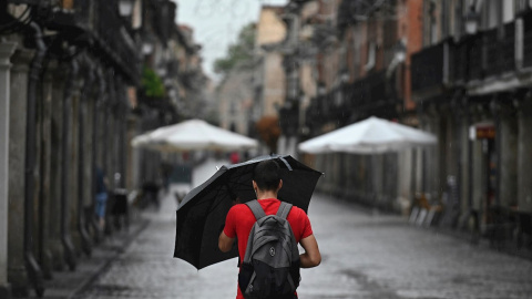 Un hombre se protege de la lluvia que cae en Alcalá de Henares.