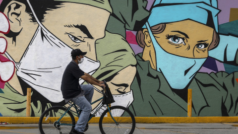 Un hombre pasa en bicicleta frente a un mural en Ciudad Juárez.