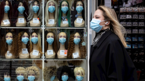 Una mujer ataviada con máscara sanitaria pasa frente a un escaparate este miércoles en París. EFE