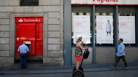 Un hombre utiliza un cajero automático del Banco Santander junto a una oficina del Popular, en Madrid. /Juan Medina