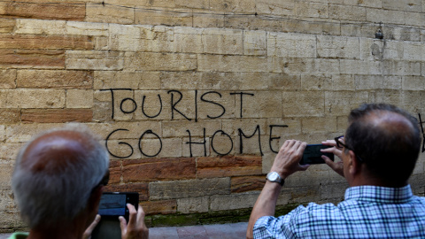 Dos personas toman una foto de una pintada contra el turismo en el centro histórico de Oviedo. REUTERS/Eloy Alonso