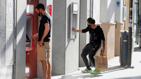 Dos jóvenes operan en sendos cajeros automáticos de dos entidades bancarias, en la localidad malagueña de Ronda. REUTERS/Jon Nazca