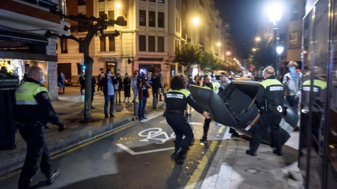 Miembros de la Policía Municipal retiran los contenedores volcados en la calzada por los participantes en las protestas que se han producido esta noche en las calles de Bilbao, por las medidas impuestas ante el aumento de contagios de Coronavirus.