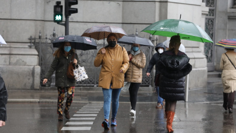 Transeúntes caminan por el centro de la capital protegiéndose de la lluvia con paraguas, en Madrid.