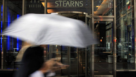 Una mujer con paraguas pasa junto a la entrada a la sede de Bear Stearns en Nueva York. AFP