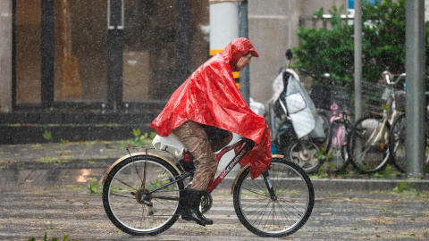 Un hombre pedalea en bicicleta entre la lluvia y el viento provocadas por el tifón Bebinca este lunes en Shanghai (China).