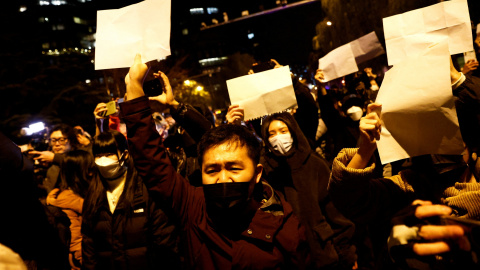 Manifestantes se concentran y sostienen hojas de papel blancas en protesta por las restricciones 'covid zero', mientras homenajean a las víctimas de un incendio en Urumqi (China)