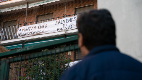 Ángel, vecino de Puerta del Ángel, mira la pancarta de un vecino con el lema "Salvemos el barrio".