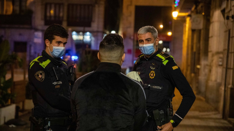 Una pareja de la Guardia Urbana multa a una persona tras la entrada en vigor del toque de queda, a 24 de diciembre de 2021, en Barcelona, Catalunya (España).