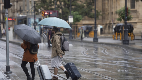 Una pareja con maletas se protegen de la lluvia bajo sus paraguas. A 21 de octubre de 2022, en Sevilla (Andalucía, España).