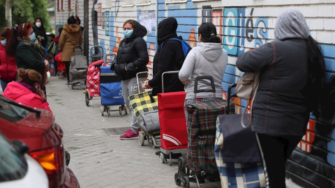 Varias personas esperan en la fila para recoger alimentos proporcionados por la Asociación de vecinos de Aluche. EFE