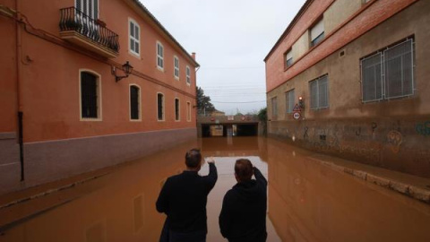 Dos hombres observan el acceso a un paso inferior de la vía ferroviaria inundado por el temporal que afectó en la localidad valenciana de Carcaixent.