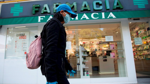 Imagen de archivo de una viandante, protegida con guantes y mascarilla, pasa por delante de una farmacia.