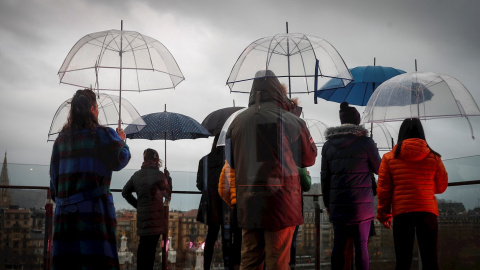 Varias personas se protegen de la lluvia con sus paraguas este miércoles en la terraza del centro cultural Tabakalera de San Sebastián