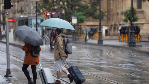 Una pareja con maletas se protegen de la lluvia bajo sus paraguas en Sevilla-21/10/2022