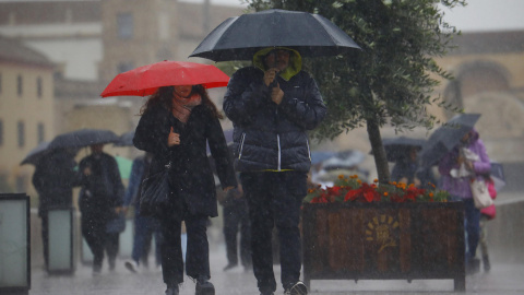 Unas personas se protegen con paraguas de la lluvia mientras caminan por el puente romano de Córdoba en una jornada en la que la ciudad se encuentra en aviso amarillo por lluvias.