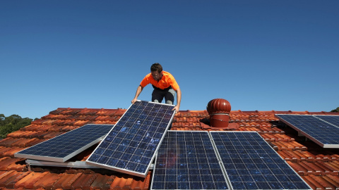 Un operario trabaja colocando paneles solares en un tejado de una vivienda.